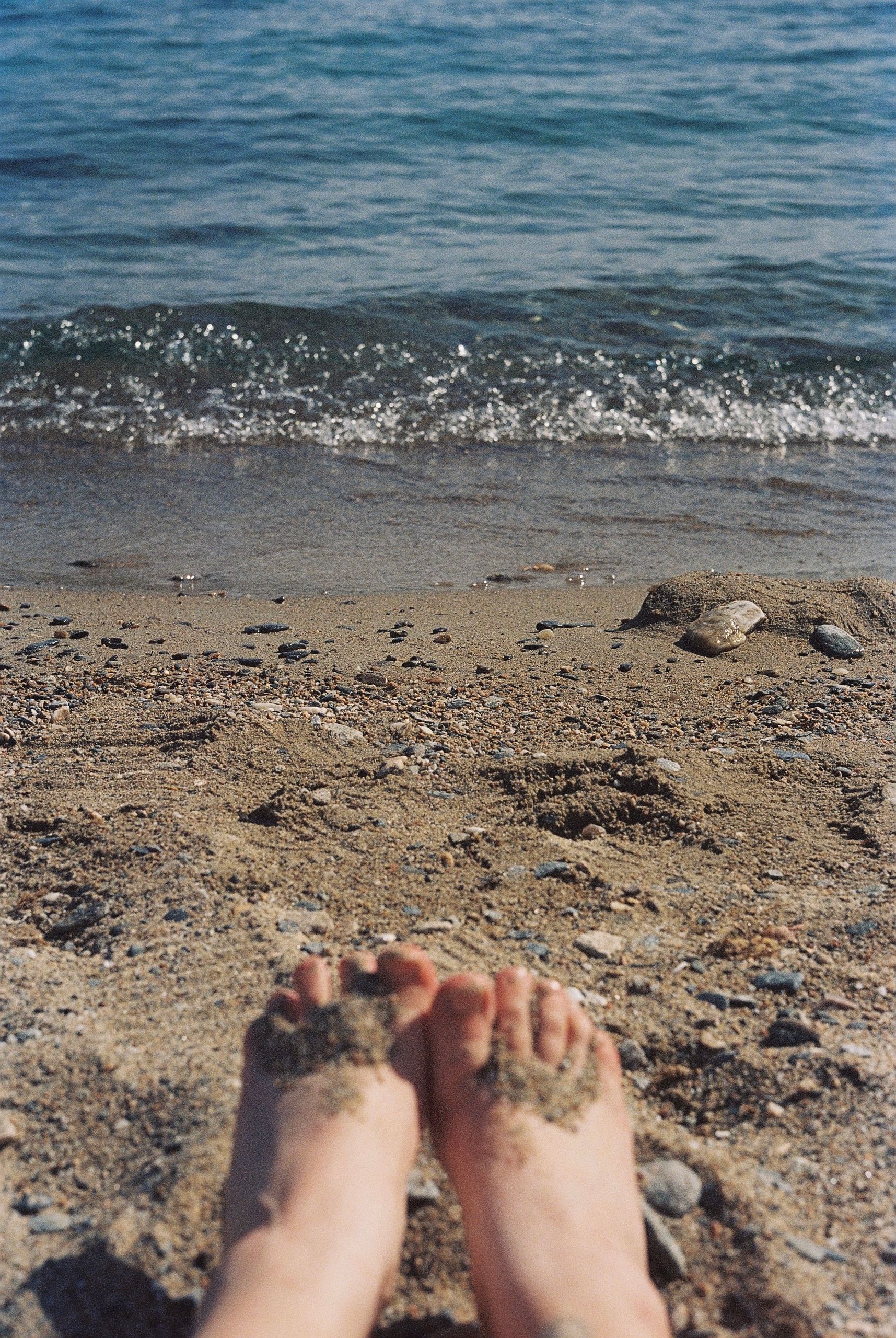 A serene beach view with sandy feet foreground and gentle waves in the background.